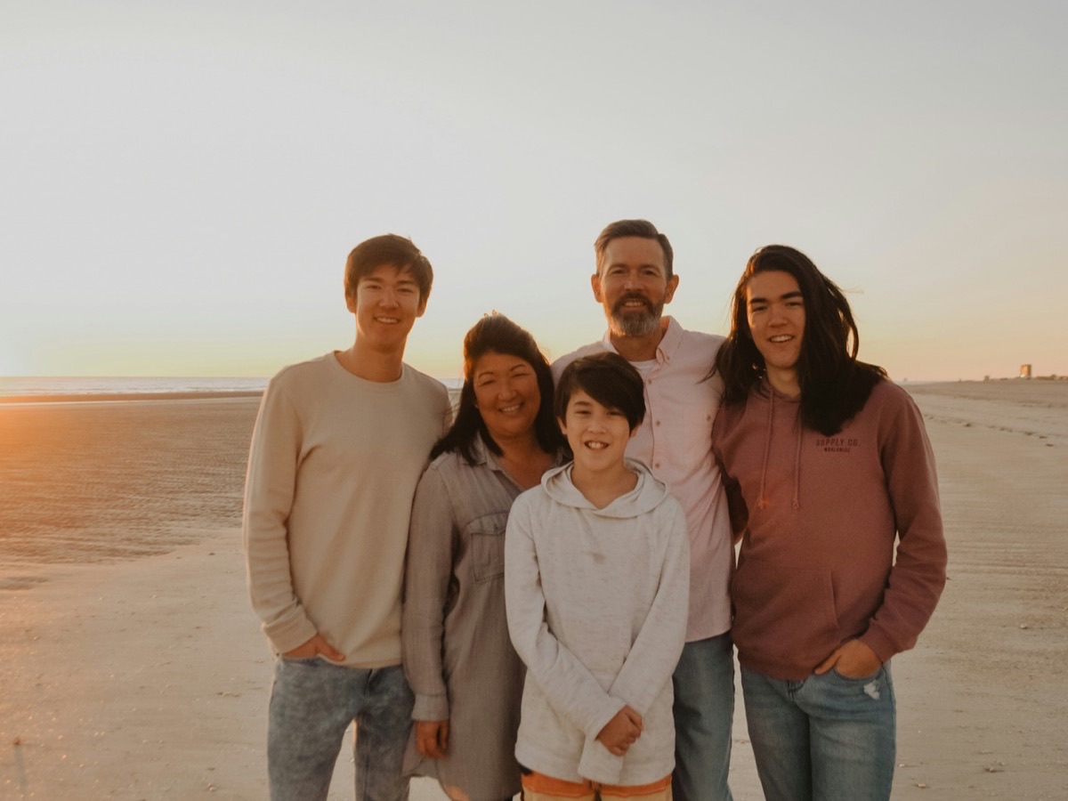Three generations of a family standing together on a beach at sunset
