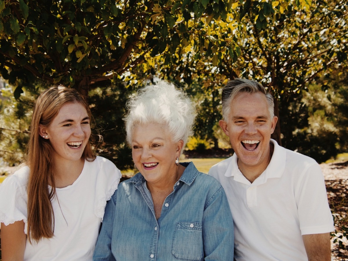 An adult daughter laughing outdoors with her mother and father